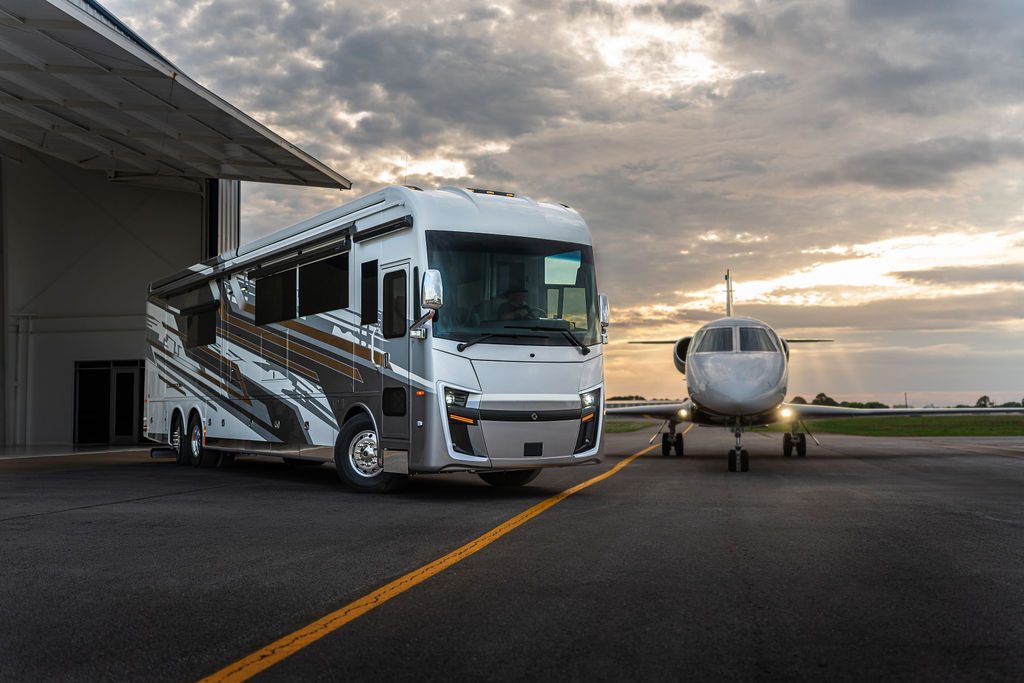 Cornerstone Series 6 luxury coach beside a private jet outside a hangar at sunset
